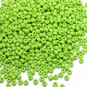 May include: A large pile of small, round, light green glass beads. The beads are all the same size and shape, and they are scattered randomly on a white background.