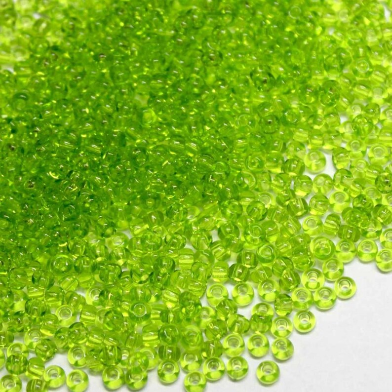 May include: A large pile of small, round, lime green glass beads. The beads are translucent and have a slight shimmer.