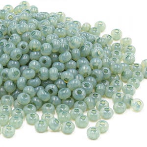 May include: A large pile of light green glass seed beads. The beads are round and have a slightly frosted finish.