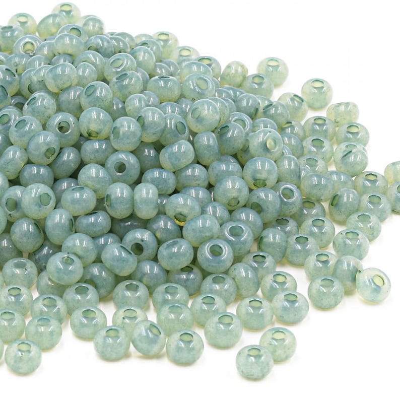 May include: A large pile of light green glass seed beads. The beads are round and have a slightly frosted finish.