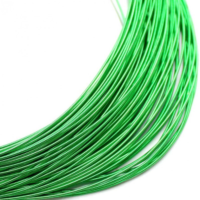 May include: A coil of bright green metallic wire featuring a textured, spiraled surface. The wire is arranged in a series of concentric loops, creating a dense, uniform pattern of vibrant green lines that curve across the frame.