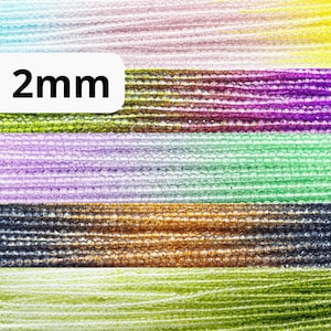 May include: A close-up of a variety of 2mm glass beads in different colors, including clear, green, purple, and brown. The beads are arranged in rows and are all the same size.