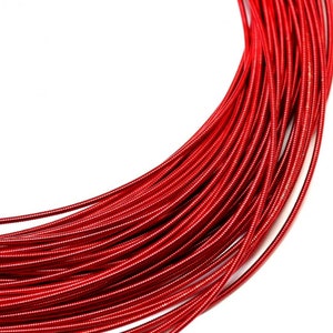May include: A coil of vibrant red craft wire featuring a smooth, metallic finish and a consistent, rounded texture. The wire is wound into a circular shape, showcasing its flexible nature and bright, uniform color throughout the entire length.