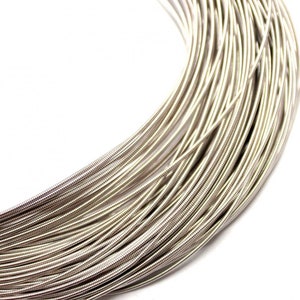 May include: A coiled length of silver-colored metal wire featuring a tightly wound, textured surface. The wire is arranged in a series of concentric loops, creating a dense, uniform pattern of metallic strands that reflect light across the surface.