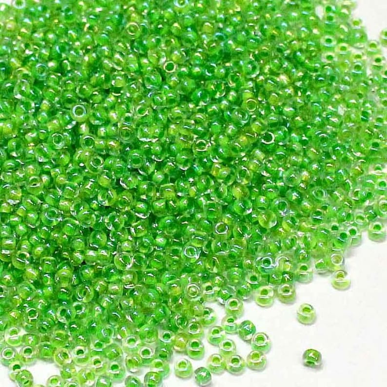 May include: A large pile of small, round, green glass beads with a slight iridescent sheen.