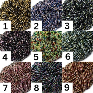 Op de afbeelding: Negen verschillende kleuren glazen kralen, elk in een aparte stapel. De kralen zijn klein en rond en hebben een glanzende, iriserende afwerking.