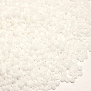 Peut inclure: Un grand tas de perles de rocaille blanches. Les perles sont petites et rondes, avec un trou au centre. Elles sont parfaites pour la fabrication de bijoux ou d'autres projets d'artisanat.
