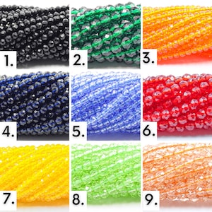 May include: Nine different colors of faceted glass beads. The beads are small and round, and they are arranged in rows. The colors are black, green, orange, blue, red, yellow, light green, and peach.