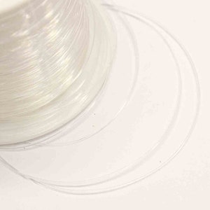 May include: A spool of clear, iridescent fishing line. The line is wound tightly around the spool and is ready to be used for fishing.