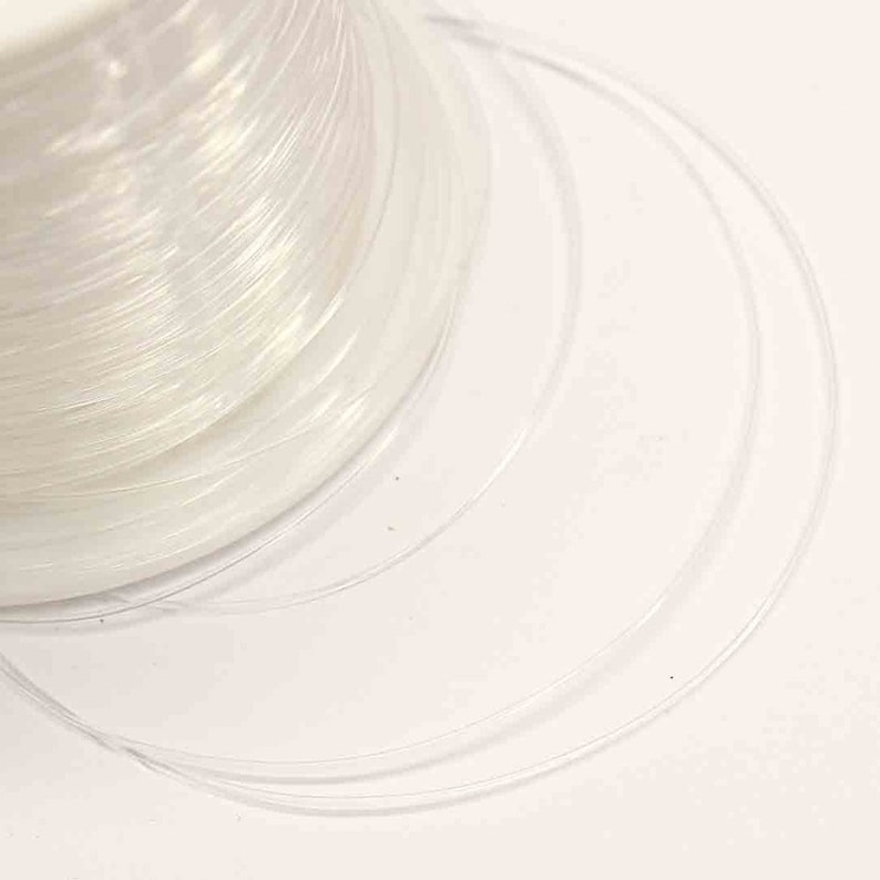 May include: A spool of clear, iridescent fishing line. The line is wound tightly around the spool and is ready to be used for fishing.