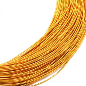 May include: A coil of metallic gold-colored wire featuring a tightly wound, ribbed texture along its entire length. The wire is arranged in a curved, overlapping bundle, showcasing a consistent, bright, reflective finish across every strand.