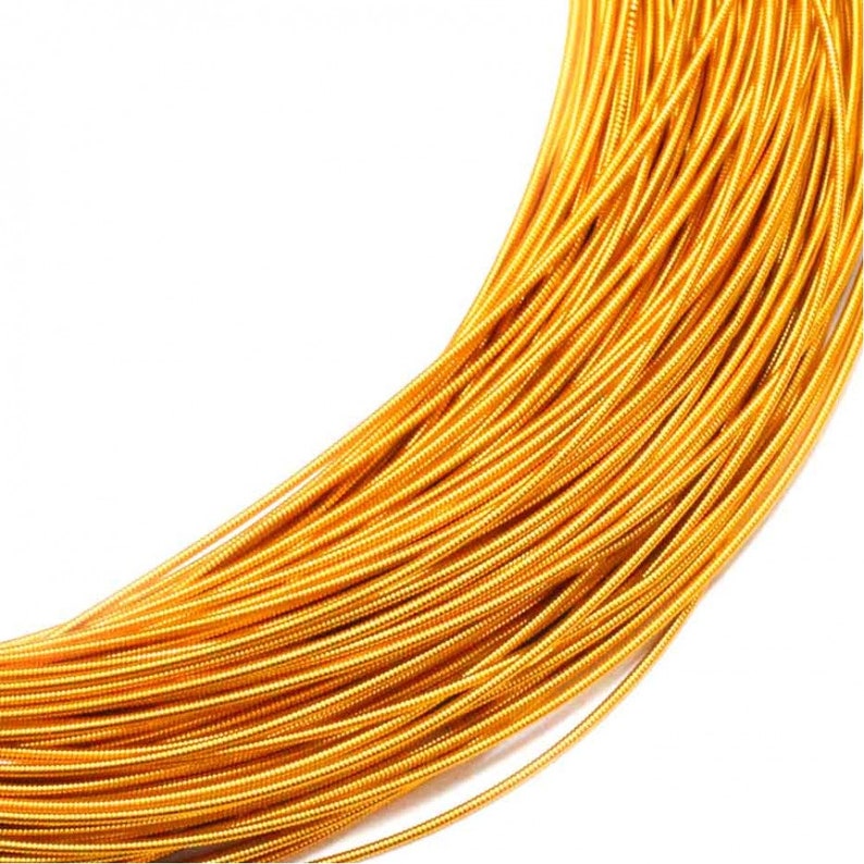 May include: A coil of metallic gold-colored wire featuring a tightly wound, ribbed texture along its entire length. The wire is arranged in a curved, overlapping bundle, showcasing a consistent, bright, reflective finish across every strand.
