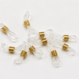 May include: A collection of clear silicone eyeglass chain connectors featuring gold-toned metal coils. Each connector consists of a flexible loop designed to hold eyewear arms, secured by a sliding metallic spring component for adjustment.
