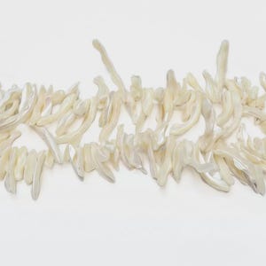 Può includere: Primo piano di una collana di perline irregolari bianche. Le perline hanno una lucentezza perlescente e sono disposte su uno sfondo bianco. Le perline sembrano essere fatte di un materiale naturale.