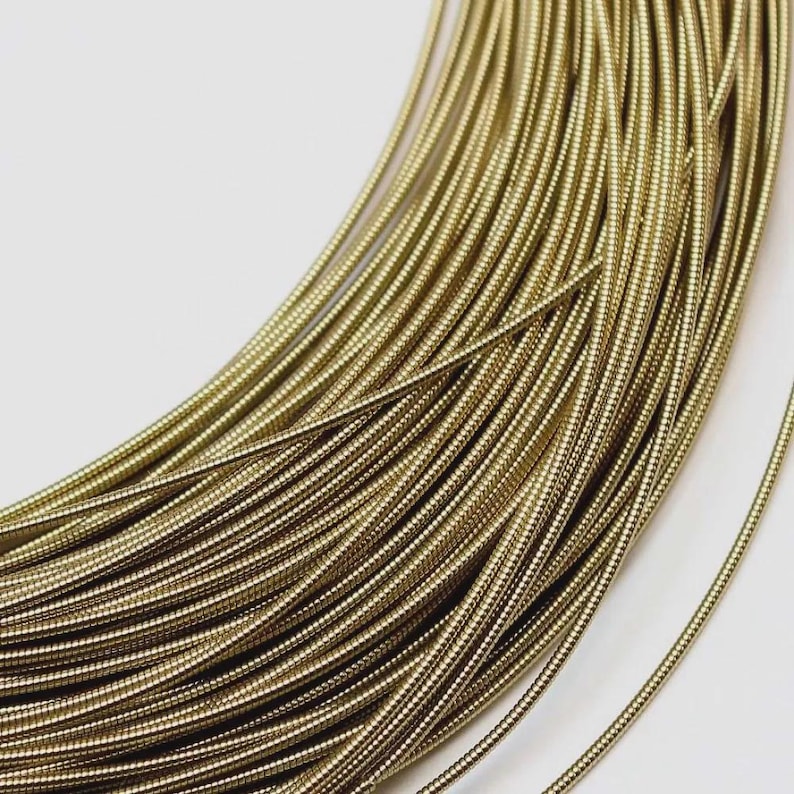 May include: A coil of metallic gold-colored wire featuring a tightly wound, ribbed, or coiled texture along its entire length. The wire is arranged in a circular pattern, showing multiple parallel strands of the same uniform, textured material.