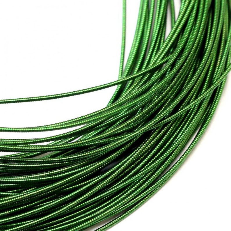 May include: A coil of flexible, metallic green craft wire featuring a continuous, tightly wound spiral texture along its entire length. The wire is arranged in multiple overlapping loops, showcasing a bright, reflective, and uniform emerald green finish.