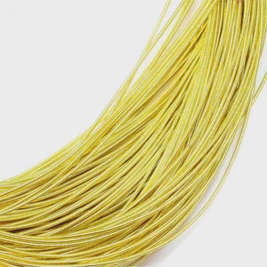 May include: A coiled length of metallic gold wire featuring a fine, spiraled texture along its entire surface. The wire is arranged in a series of overlapping, curved loops that create a dense, uniform pattern of bright, reflective yellow-gold.
