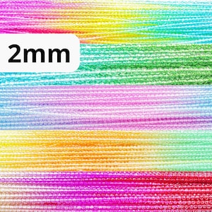 May include: Assortment of 2mm iridescent glass seed beads in various colours, including pink, green, blue, and yellow. The beads are arranged in rows, creating a rainbow effect.