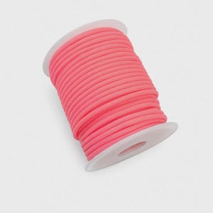 Puede incluir: Una bobina de cordón elástico de color rosa neón brillante enrollado cuidadosamente alrededor de un cilindro de plástico blanco. El cordón es liso y redondeado, con un grosor constante en toda la longitud de la bobina, creando un aspecto vibrante y uniforme.