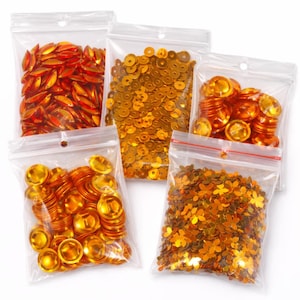 Può includere: Cinque sacchetti di plastica trasparente pieni di vari materiali per l'artigianato color oro. I sacchetti contengono paillettes, gemme a forma di goccia e abbellimenti rotondi e bombati. Ideale per scrapbooking, creazione di biglietti o altri progetti di artigianato.
