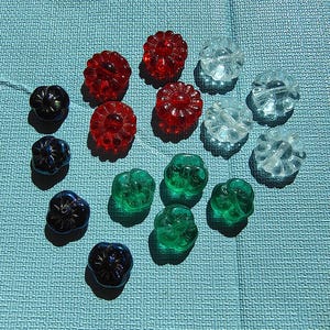 May include: Assortment of glass buttons in various colors, including red, green, blue, and clear. The buttons are shaped like flowers with multiple petals.