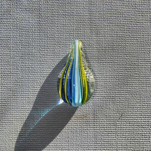 May include: A teardrop-shaped glass pendant with blue, white, and yellow stripes.