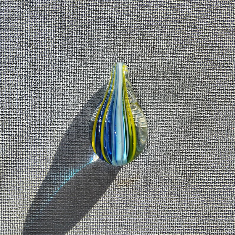 May include: A teardrop-shaped glass pendant with blue, white, and yellow stripes.