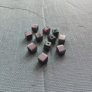 May include: A collection of purple and black square-shaped beads. The beads have a marbled effect and are scattered on a gray textured surface.