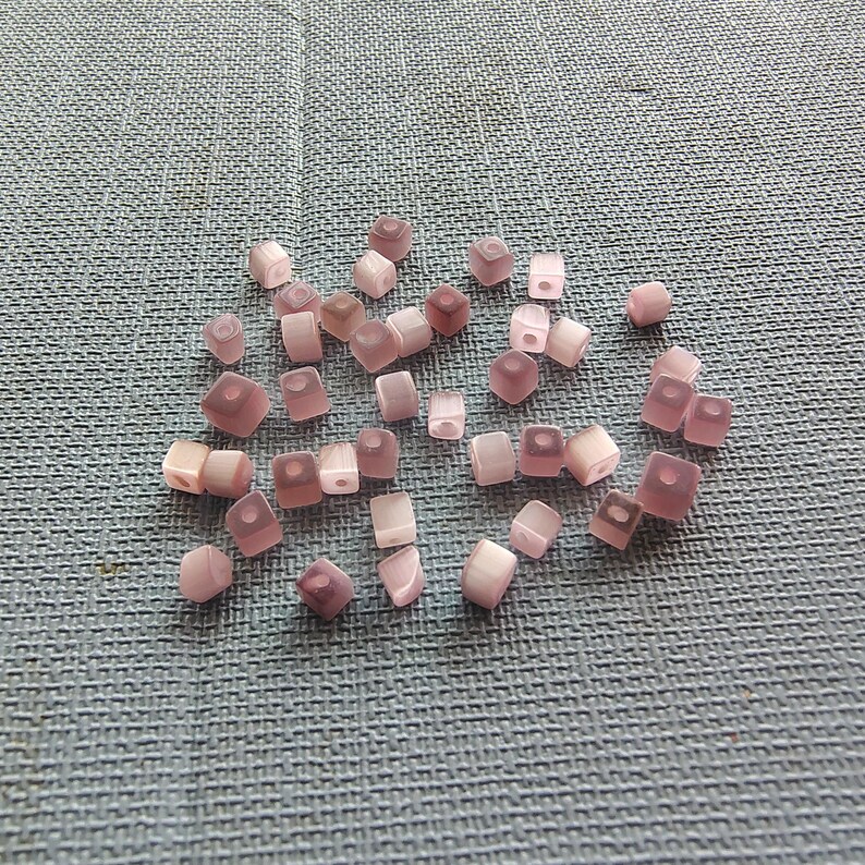 May include: A group of small, square, translucent pink beads with a white iridescent sheen.