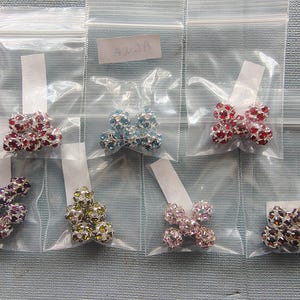 May include: Assortment of sparkling rhinestone beads in various colors, including red, blue, purple, green, pink, and brown, packaged in clear plastic bags. Each bead is a cluster of smaller rhinestones, creating a dazzling effect. Ideal for jewelry making.