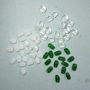 May include: Assortment of glass beads in three colors: white, clear, and green. The beads are oval shaped and have a smooth, polished finish.