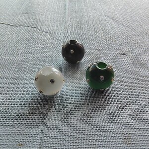 May include: Three round beads with rhinestones. The beads are black, white, and green.
