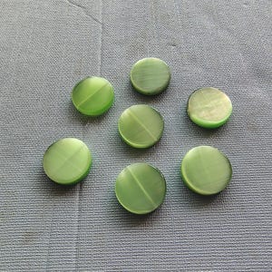 May include: Seven green round buttons with a smooth, shiny finish. The buttons have a subtle, light green color and a slightly raised center.