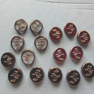 May include: A collection of decorative buttons with a copper-colored rim and a tree design. Some buttons have a clear center, others are red or black. The tree design is in a metallic gold color.