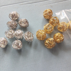 May include: A collection of wire sphere beads in silver and gold. The silver beads are arranged in a group on the left, while the gold beads are on the right, some in a clear plastic bag. These decorative beads are suitable for jewelry making.