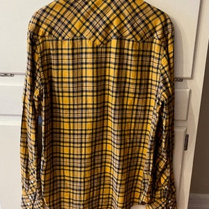 Puede incluir: Una camisa de manga larga a cuadros amarillos y negros con cuello puntiagudo y un bolsillo en el pecho.