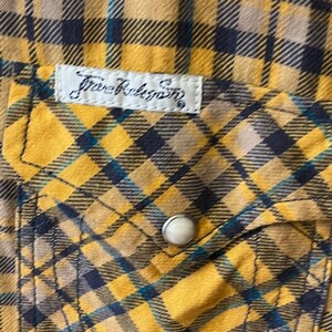 Puede incluir: Camisa de franela a cuadros amarillos y negros con una peque&ntilde;a etiqueta blanca que dice "True Religion" en una fuente de escritura negra.