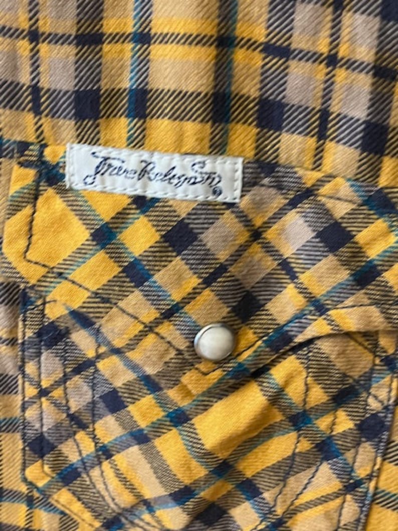 Puede incluir: Camisa de franela a cuadros amarillos y negros con una peque&ntilde;a etiqueta blanca que dice "True Religion" en una fuente de escritura negra.