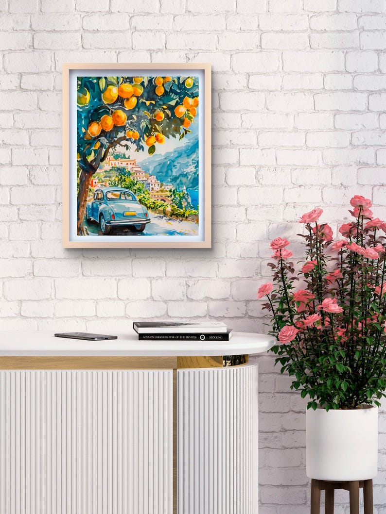 May include: Watercolor painting in a light wood frame. The artwork depicts a blue vintage car on a road, under an orange tree, with a coastal town in the background. The painting has a bright, sunny aesthetic.