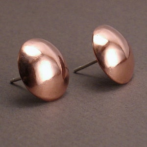 May include: A pair of copper stud earrings with a rounded, domed shape. The earrings are a shiny, metallic copper color.
