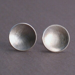 May include: A pair of silver earrings with a round, slightly concave shape. The earrings have a brushed finish.