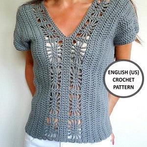 Pode incluir: Top de crochet cinza com decote em V e mangas curtas. A parte superior apresenta um delicado padrão de renda ao redor do decote e na parte da frente.  ENGLISH (US) CROCHET PATTERN
