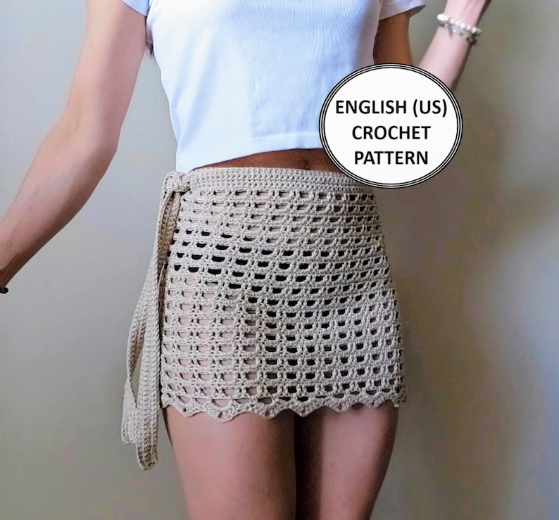 Product listing image for the Beach Blossom crochet sarong skirt pattern. A model wears the beige mesh wrap-around mini skirt with a scalloped hem. Text overlay reads: "ENGLISH (US) CROCHET PATTERN".