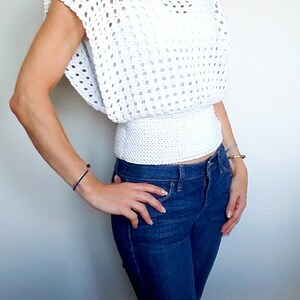 May include: White crochet top with a loose fit and a fitted elastic waistband. The top has a wide, open neckline and short sleeves.