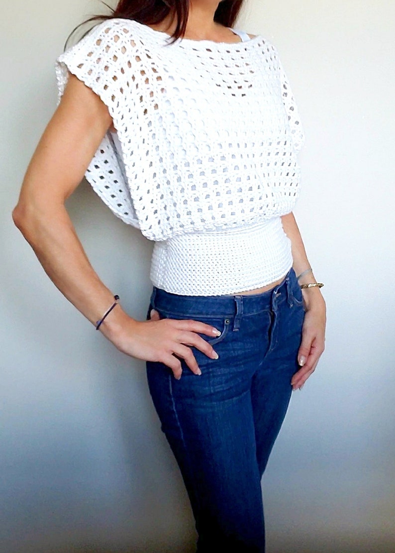 May include: White crochet top with a loose fit and a fitted elastic waistband. The top has a wide, open neckline and short sleeves.