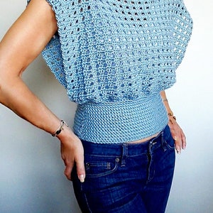 May include: A light blue crochet top with a loose fit and a fitted waist. The top has a square-shaped neckline and short sleeves.