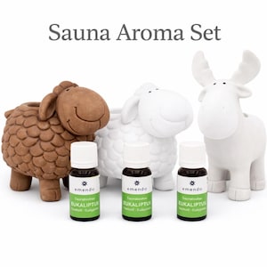 Puede incluir: Un juego de aromas para sauna con tres soportes decorativos con forma de animales: una oveja marrón, una oveja blanca y un alce blanco. Tres pequeñas botellas de aceite de eucalipto están frente a los soportes. El texto "Sauna Aroma Set" está en la parte superior.