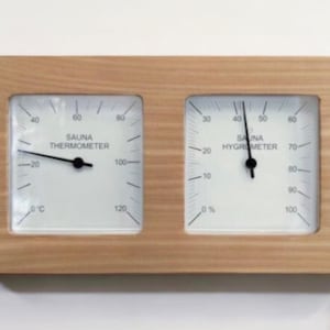 May include: A wooden framed dual dial thermometer and hygrometer for a sauna. The thermometer reads from 0 to 120 degrees Celsius and the hygrometer reads from 0 to 100 percent.