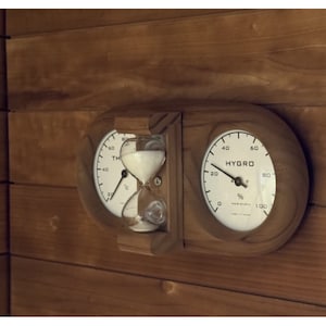 May include: A wooden panel with two round gauges and an hourglass. The left gauge is labelled "Temp" and measures in degrees Celsius. The right gauge is labelled "Hygro" and measures humidity in percent. The hourglass is made of glass and has white sand.