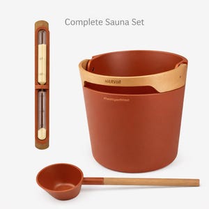 May include: Complete sauna set featuring a terracotta-colored bucket with a wooden handle, a matching ladle, and a sand timer. The bucket has the brand name "HARVIA" and the text "#healingwithheat". The timer has a cork top and bottom.